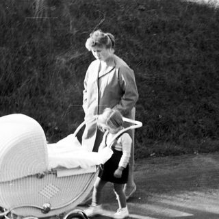 Woman pushing a vintage wicker baby carriage outdoors.
