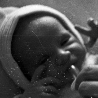 Here's a brief summary of the image: Newborn baby wrapped in cloth, held in a hand.