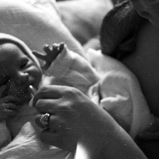 Here's a brief summary of the image: Newborn baby wrapped in cloth, held in a hand.