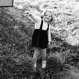 Here's a brief summary of the image: Child stands near a sign in a grassy, rural setting.
