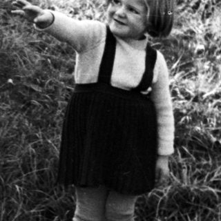 Child stands near a sign in a grassy area.