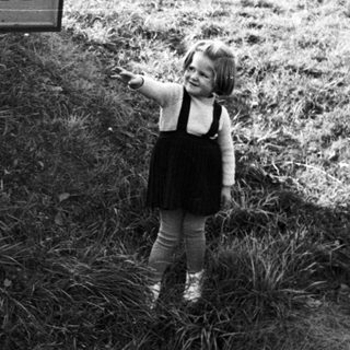 Child stands near a sign in a grassy area.