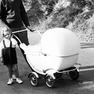 Man and child stand next to an ornate baby carriage.