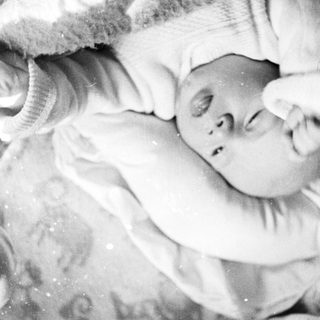 Black and white image of a baby lying in a crib.