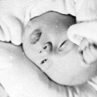 Black and white image of a baby lying in a crib.