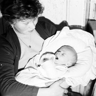 Woman holding a wrapped baby in a vintage setting.