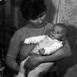 Woman holds baby, possibly in a home setting.