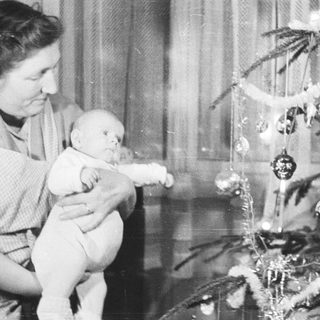 Baby being held near a decorated Christmas tree.