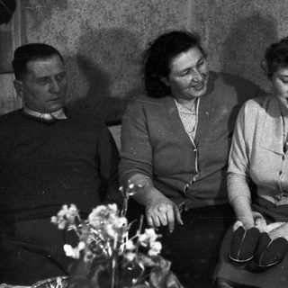 Three people sit indoors, appearing thoughtful or concerned.