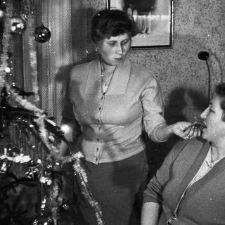 Two women appear to be smoking near a Christmas tree.