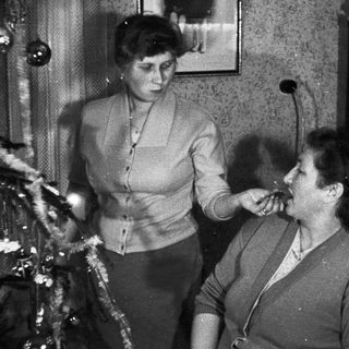 Two women appear to be smoking near a Christmas tree.