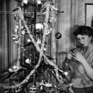 Woman decorating a small Christmas tree in a home.