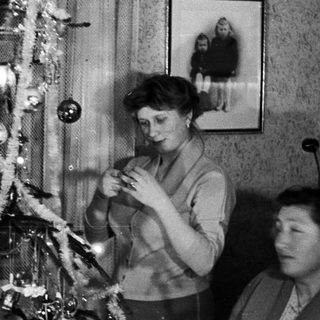 Woman decorating a small Christmas tree in a home.