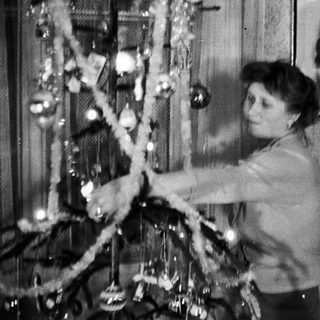 Woman decorating a Christmas tree, portrait in background.