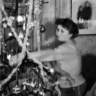 Woman decorating a Christmas tree, portrait in background.