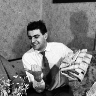 Smiling man presents flowers to a woman on a sofa.