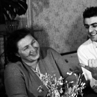 Smiling man presents flowers to a woman on a sofa.