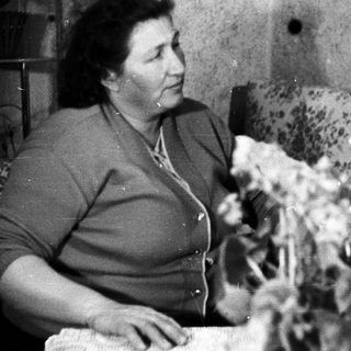 Woman sits near floral couch, holding a leafy plant.