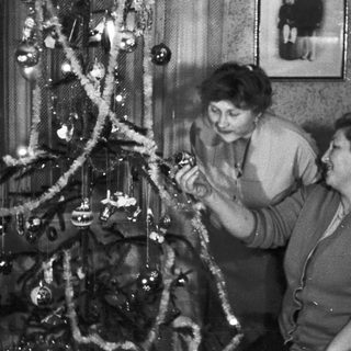 Two women decorate a Christmas tree in a vintage setting.