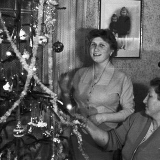 Two women decorating a Christmas tree in a vintage setting.
