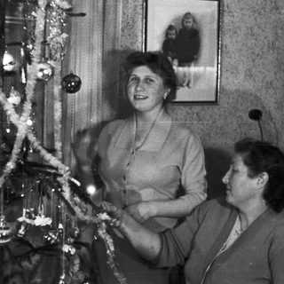 Two women decorating a Christmas tree in a vintage setting.