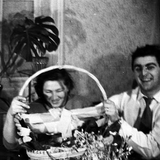 Couple smiles while holding a gift basket indoors.
