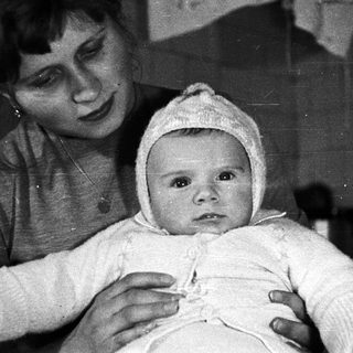 Here's a brief summary of the image: Woman holding a baby wearing a bonnet.