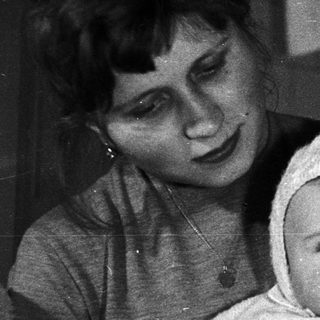 Here's a brief summary of the image: Woman holding a baby wearing a bonnet.