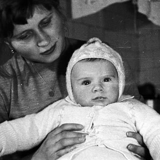 Here's a brief summary of the image: Woman holding a baby wearing a bonnet.