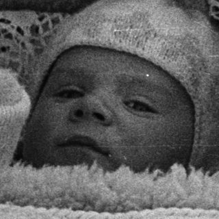 Here's a brief summary: Infant in vintage carriage, wearing a lace-trimmed bonnet.