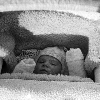 Here's a brief summary: Infant in vintage carriage, wearing a lace-trimmed bonnet.