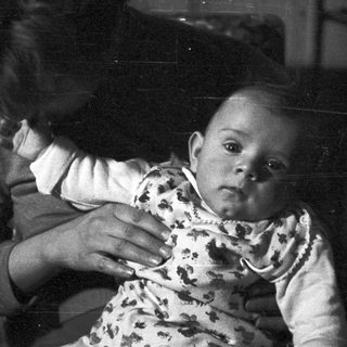 Black and white image of a baby held in someone's arms.