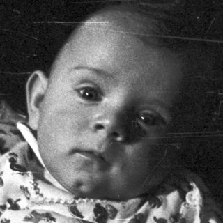Black and white image of a baby held in someone's arms.
