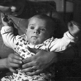 Baby being held, possibly by a parent, in black and white.
