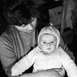 Woman holding baby wearing a bonnet, vintage photograph.