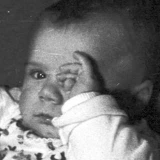 Woman holds baby, appearing in a dark, vintage photograph.