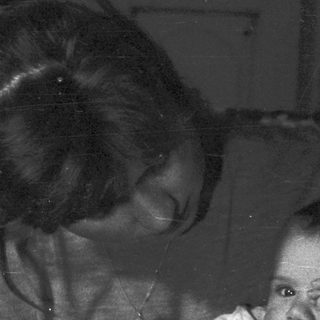 Woman holds baby, appearing in a dark, vintage photograph.