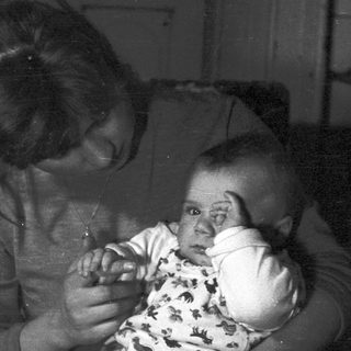 Woman holds baby, appearing in a dark, vintage photograph.