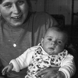 Baby held by a smiling person in a vintage photograph.