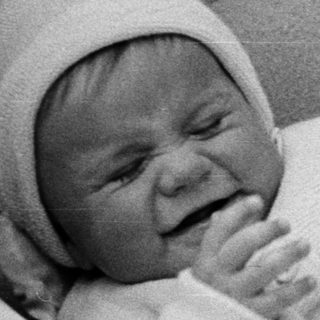 Crying baby in a vintage pram, wearing a knit outfit.