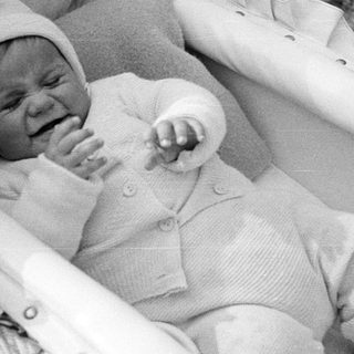 Crying baby in a vintage pram, wearing a knit outfit.
