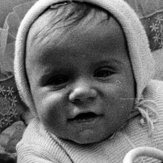 Baby in a wicker chair, wearing a knit bonnet.