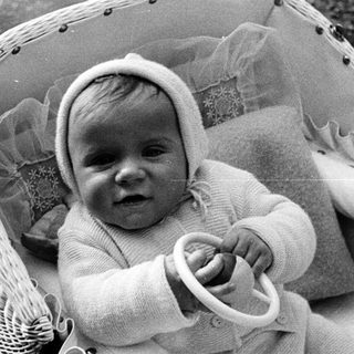 Baby in a wicker chair, wearing a knit bonnet.