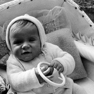 Baby in a wicker chair, wearing a knit bonnet.