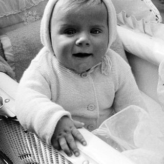 Baby in a knit outfit sits in a woven carrier.