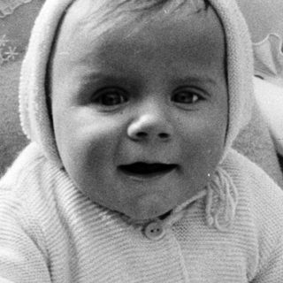 Baby in a knit outfit sits in a woven carrier.