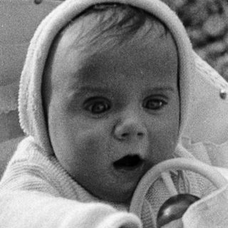 Baby in a basket, wearing a bonnet, looking forward.