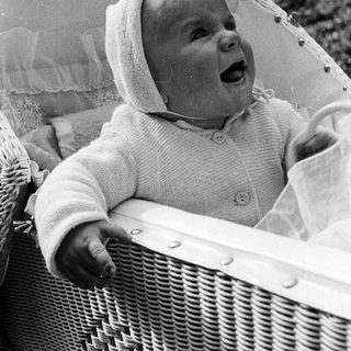 Baby in a hooded sweater sits in a wicker chair.