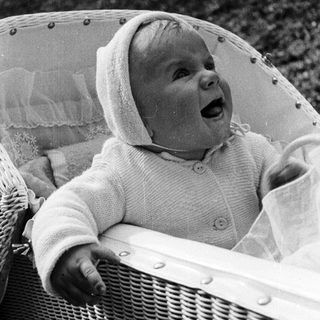 Baby in a hooded sweater sits in a wicker chair.