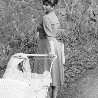 Woman stands with vintage baby carriage outdoors.